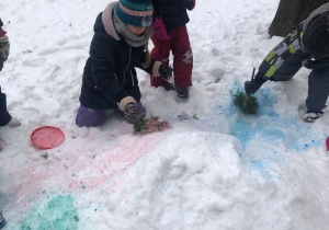 Dzieci przy użyciu naturalnych gałązek malowały farbami na śniegu